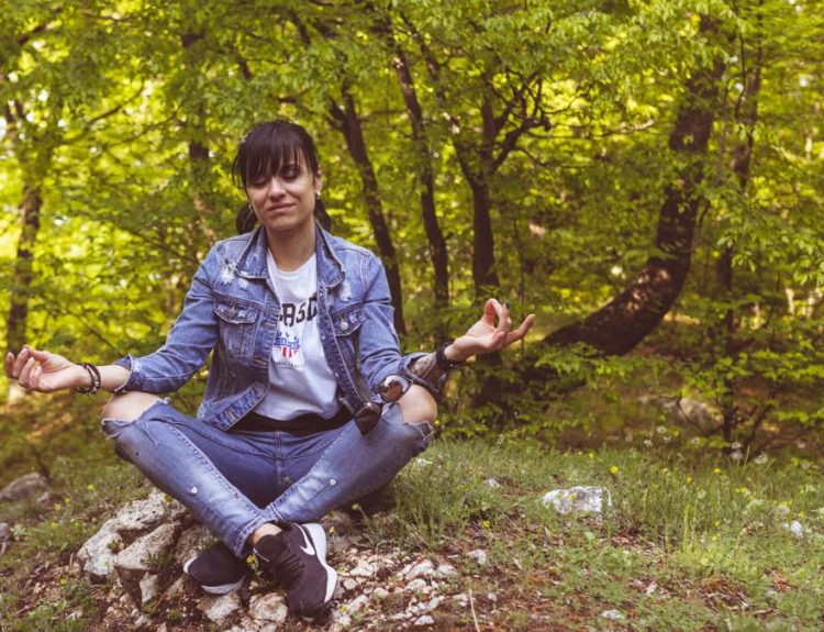 A woman meditates peacefully in a lush green forest, exuding calm and relaxation.